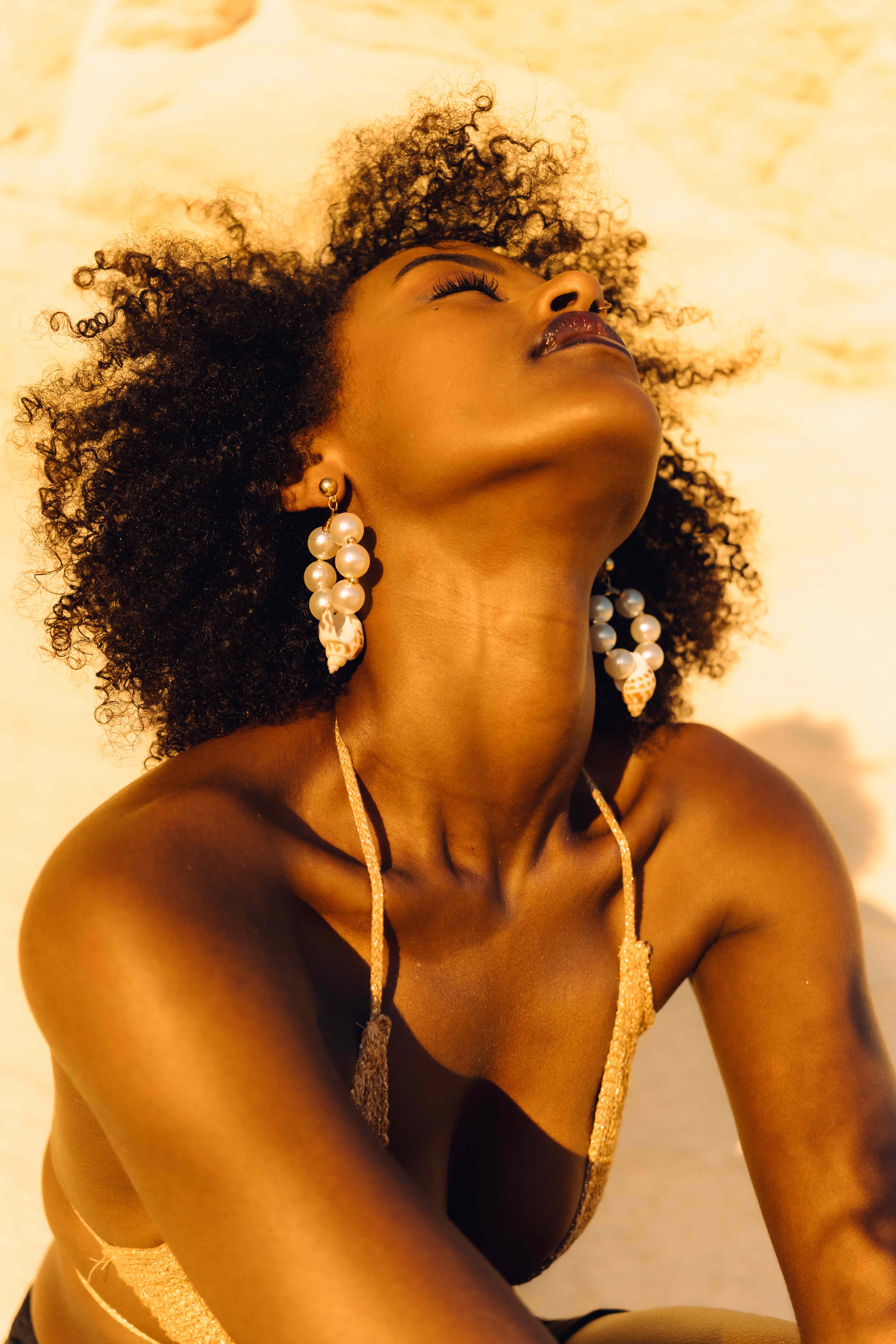 Model with head thrown back to the sun, wearing long pearl and seashell drop earrings
