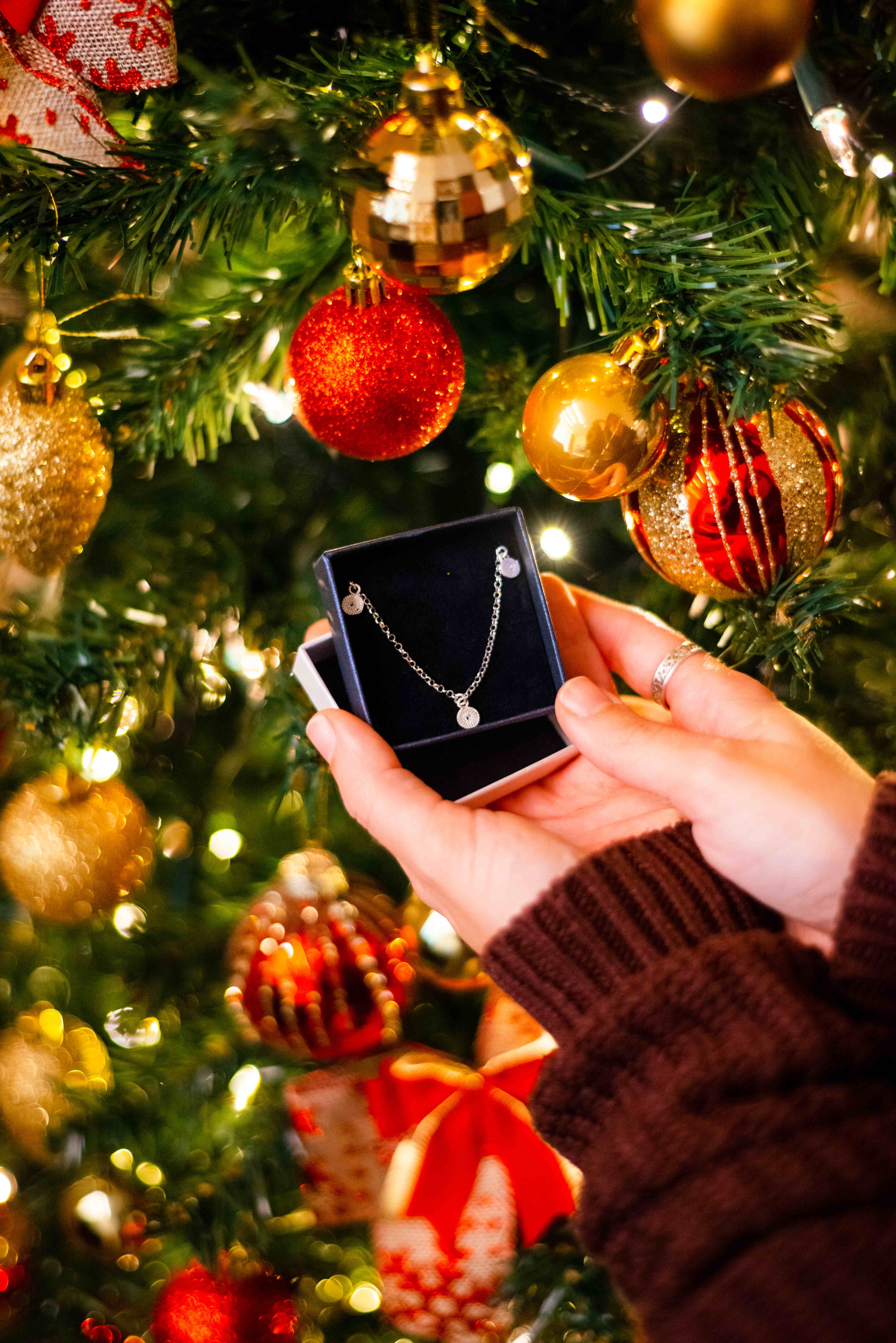 Hand holding an open jewellery box with a filigree necklace in front of a lit Christmas tree
