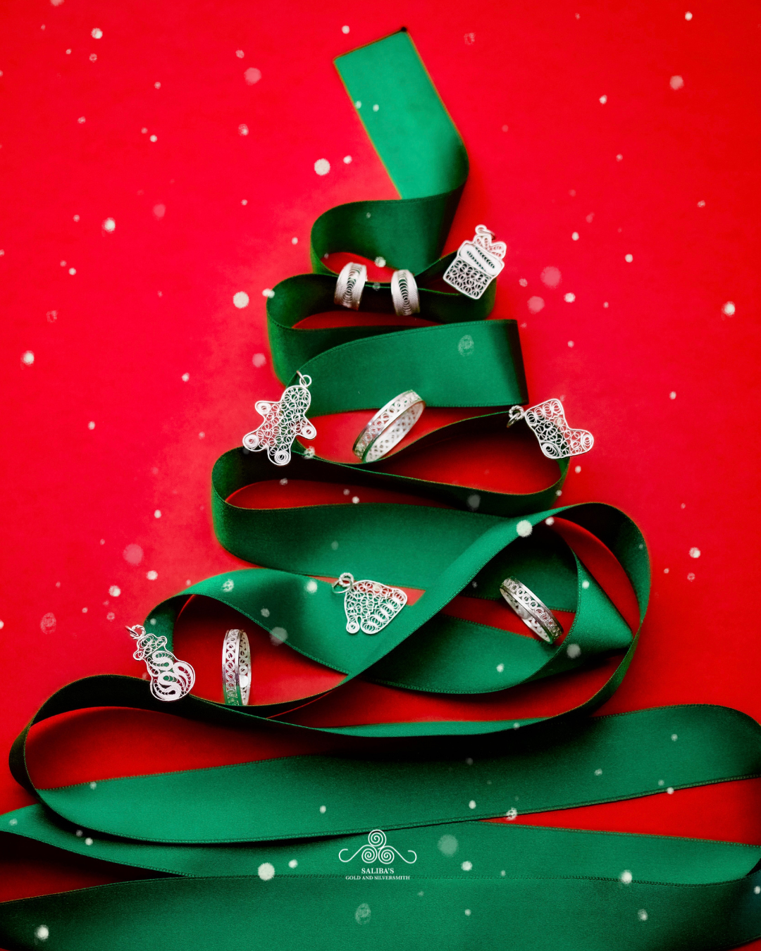 Green ribbon shaped into a Christmas tree dotted with filigree rings and charms on a red ground