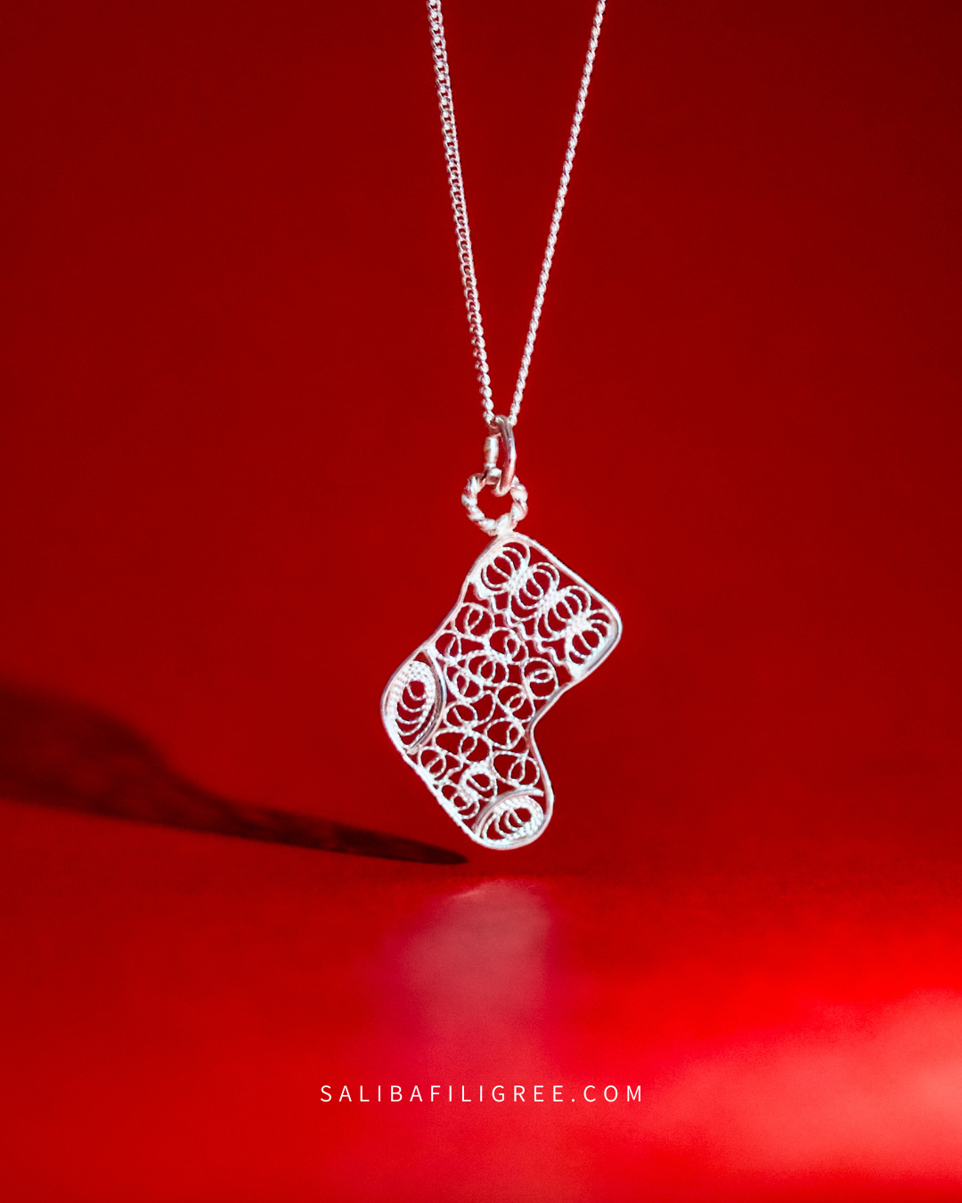 Silver filigree Christmas stocking pendant on a fine chain against a red backdrop