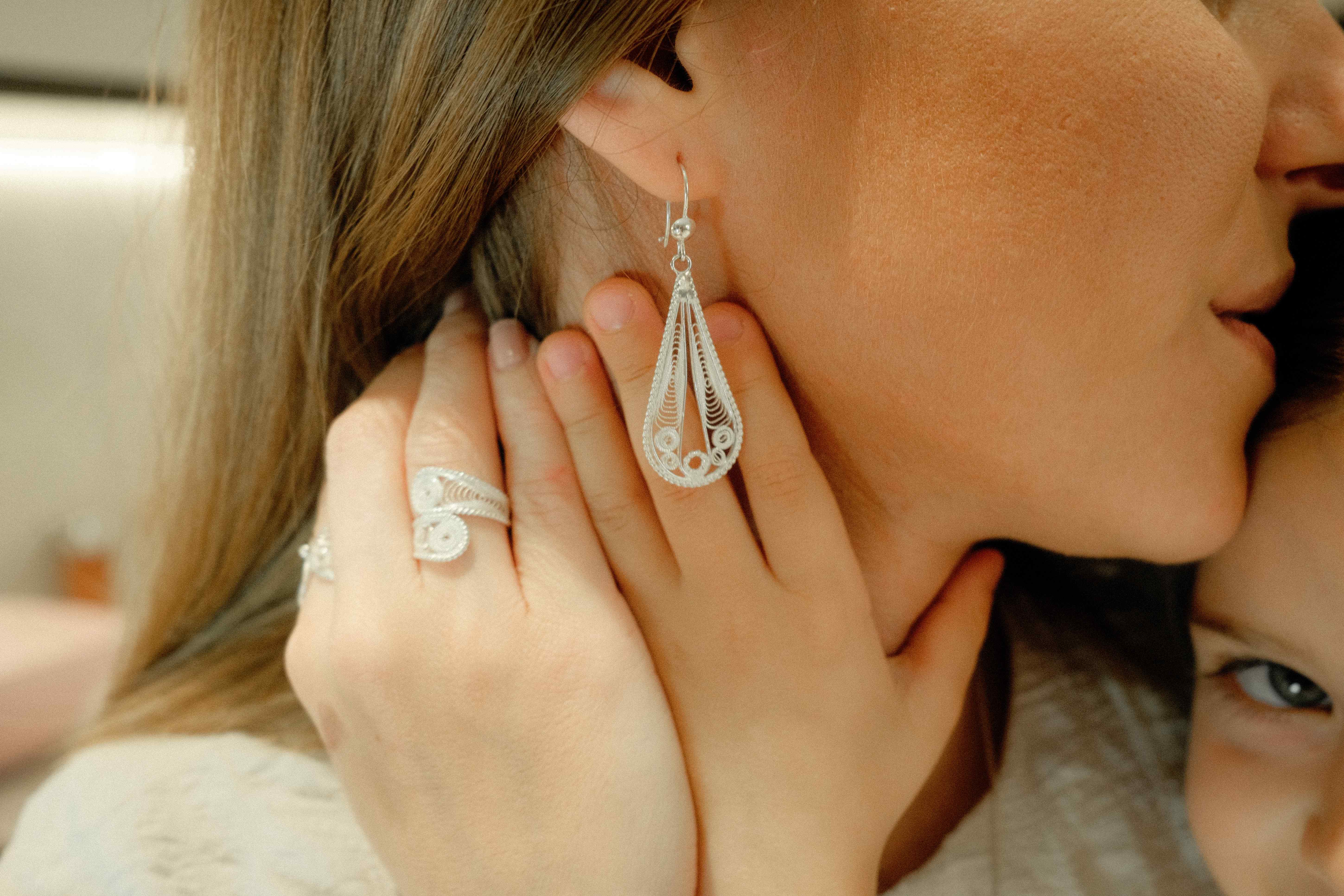 Hand resting at the jaw wearing a filigree ring beside a long teardrop filigree earring