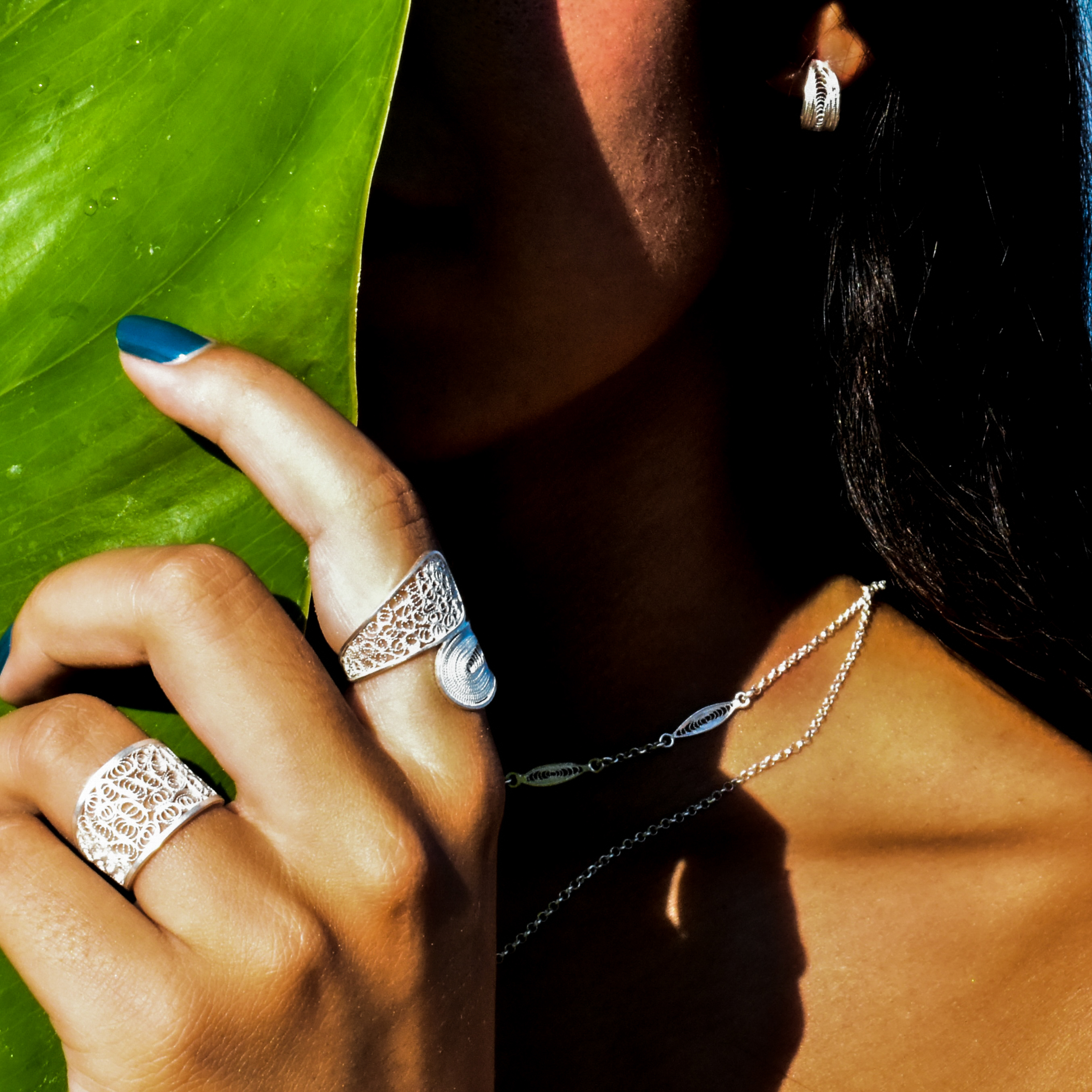 Hand with silver filigree rings against a large green leaf, a fine silver chain at the neck