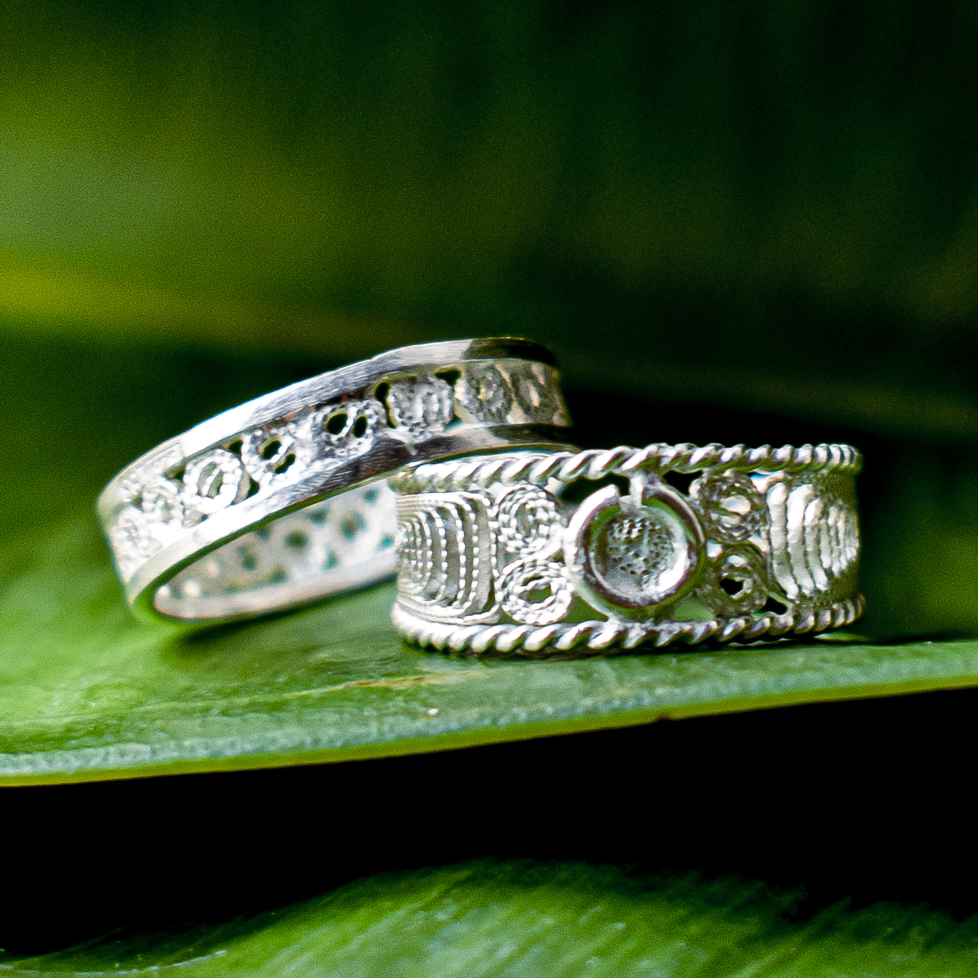 Two filigree silver bands resting on a glossy green leaf
