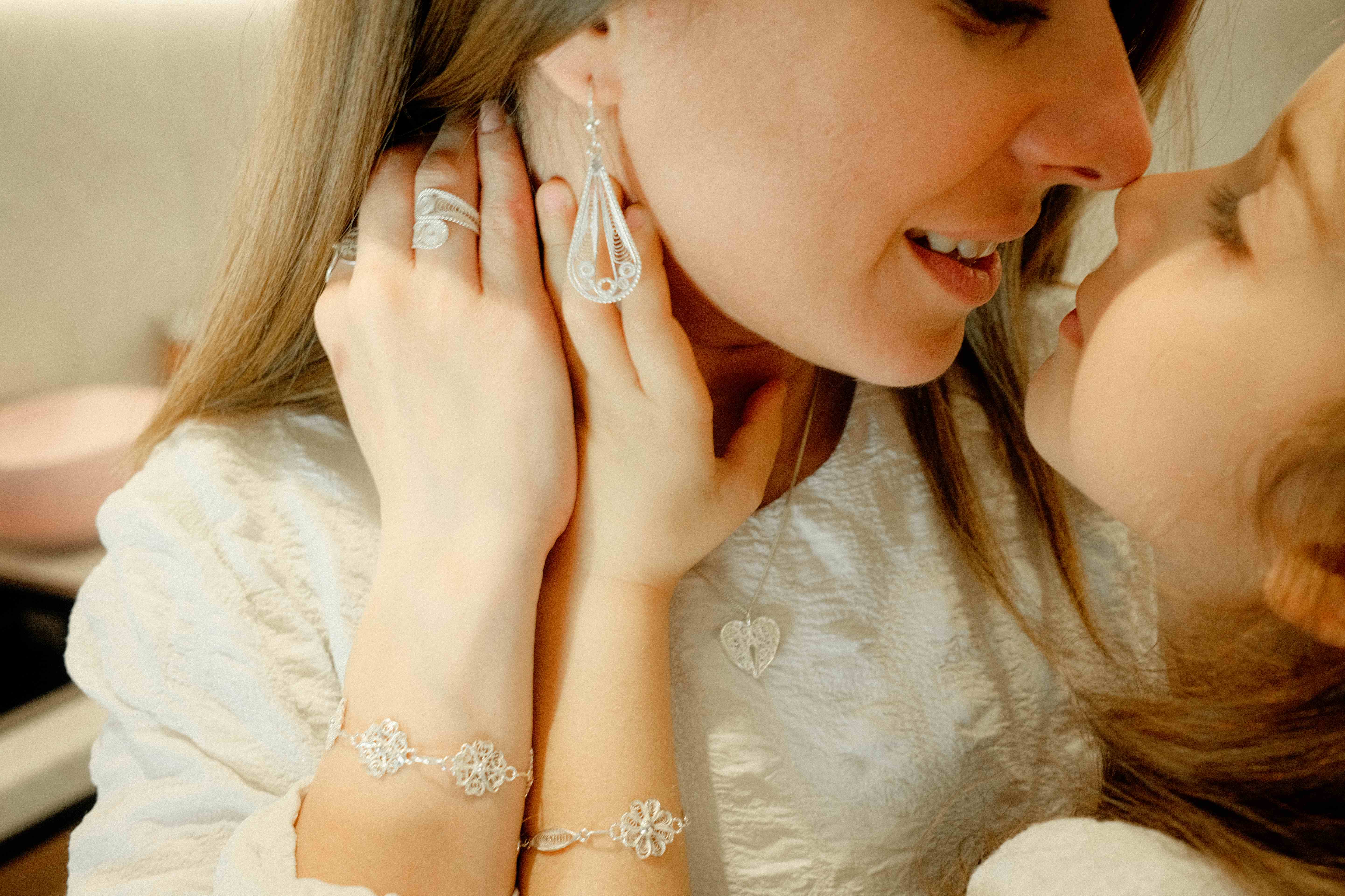 Daughter kissing her mother, filigree teardrop earring, rings, heart pendant and flower bracelets visible