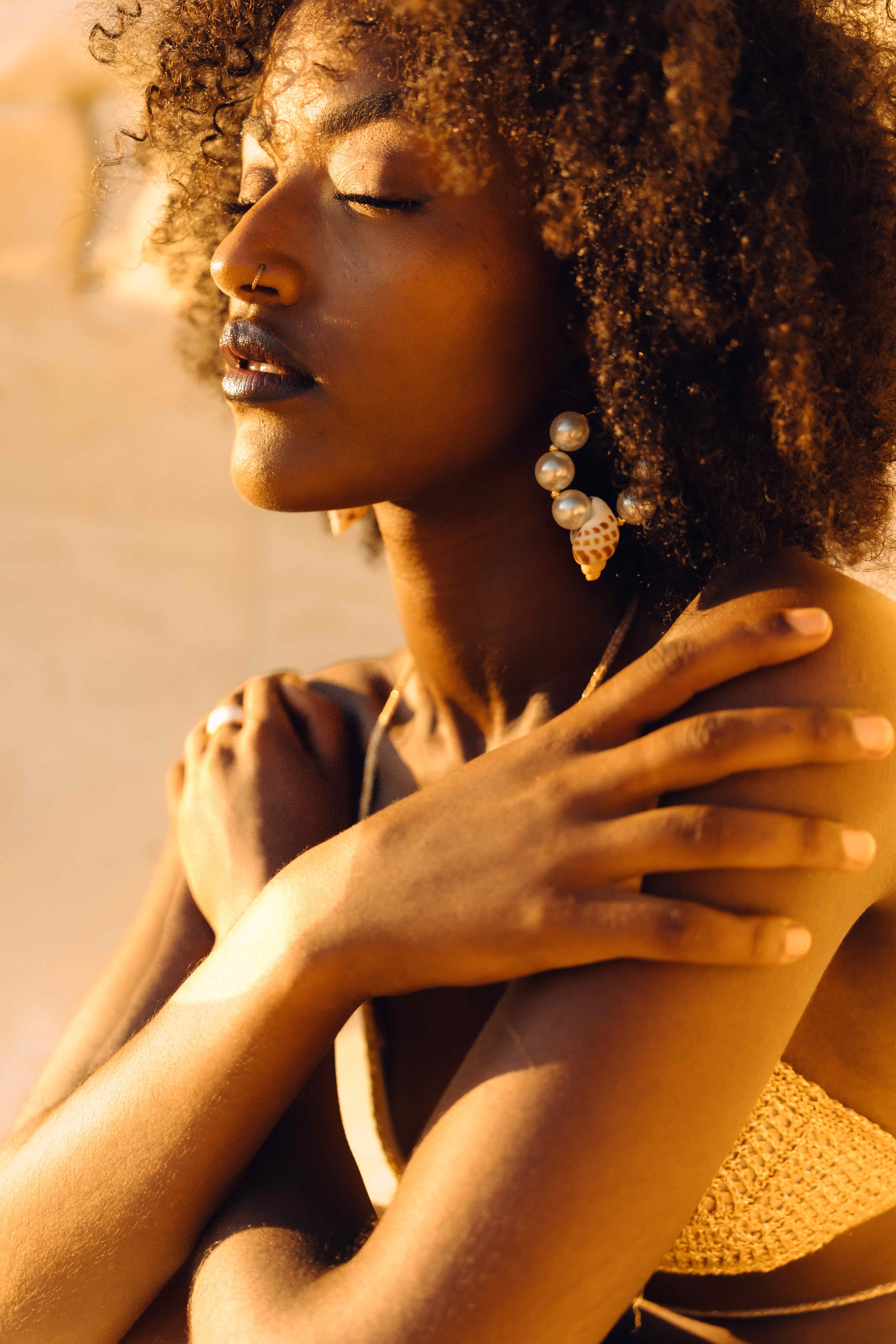 Golden-hour portrait of a woman with an afro wearing a pearl and seashell earring
